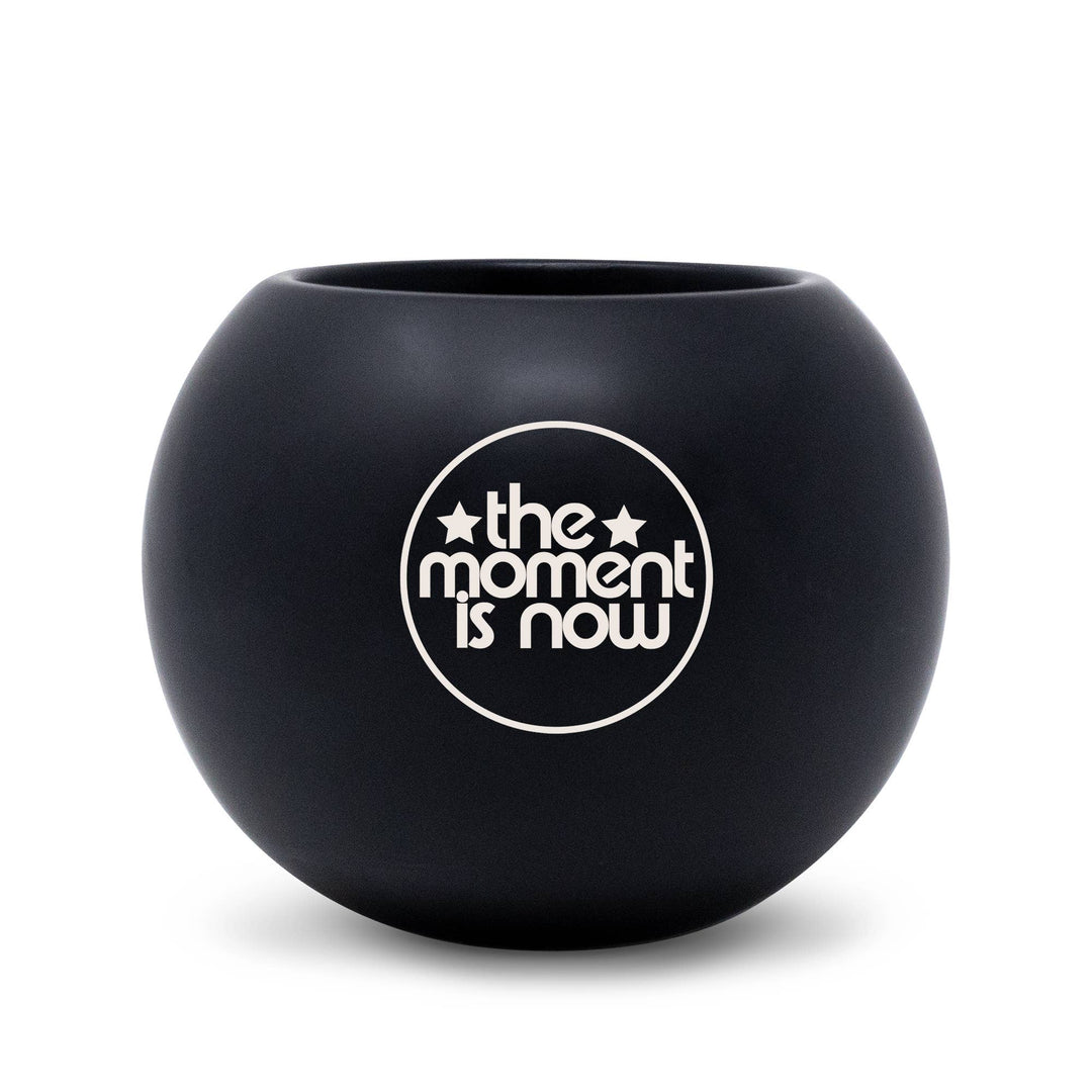 Black spherical container with 'the moment is now' text on a white background