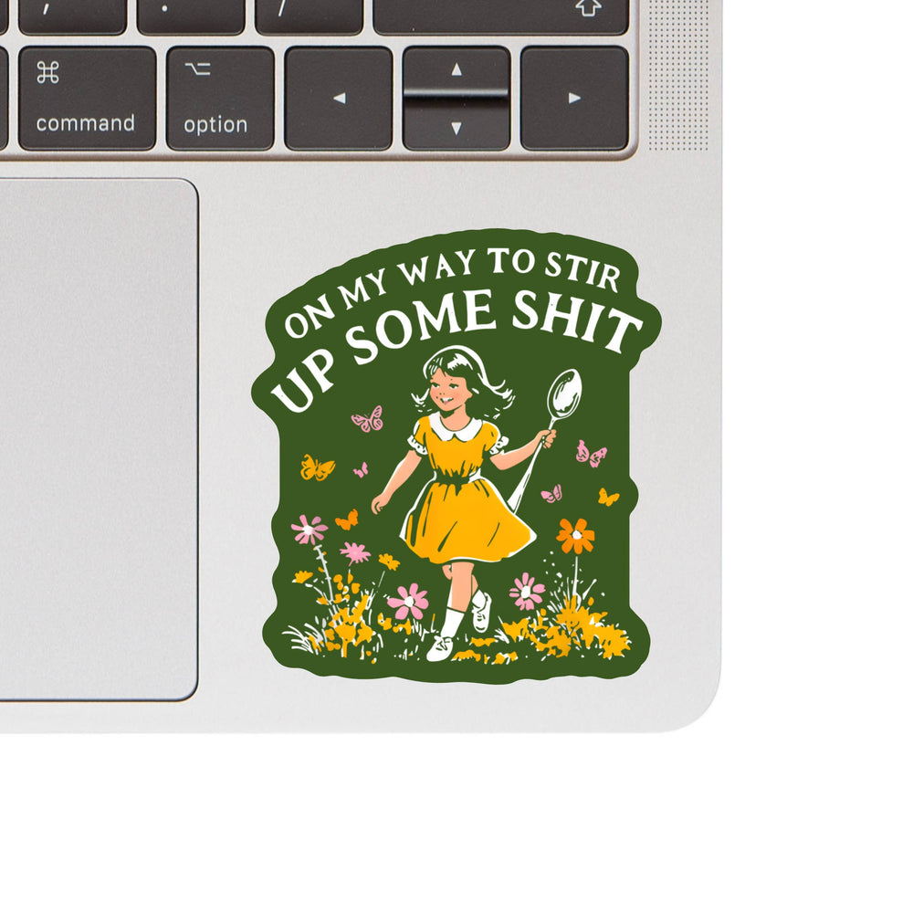 Laptop with a sticker of a girl holding a spoon surrounded by flowers and text on a green background.